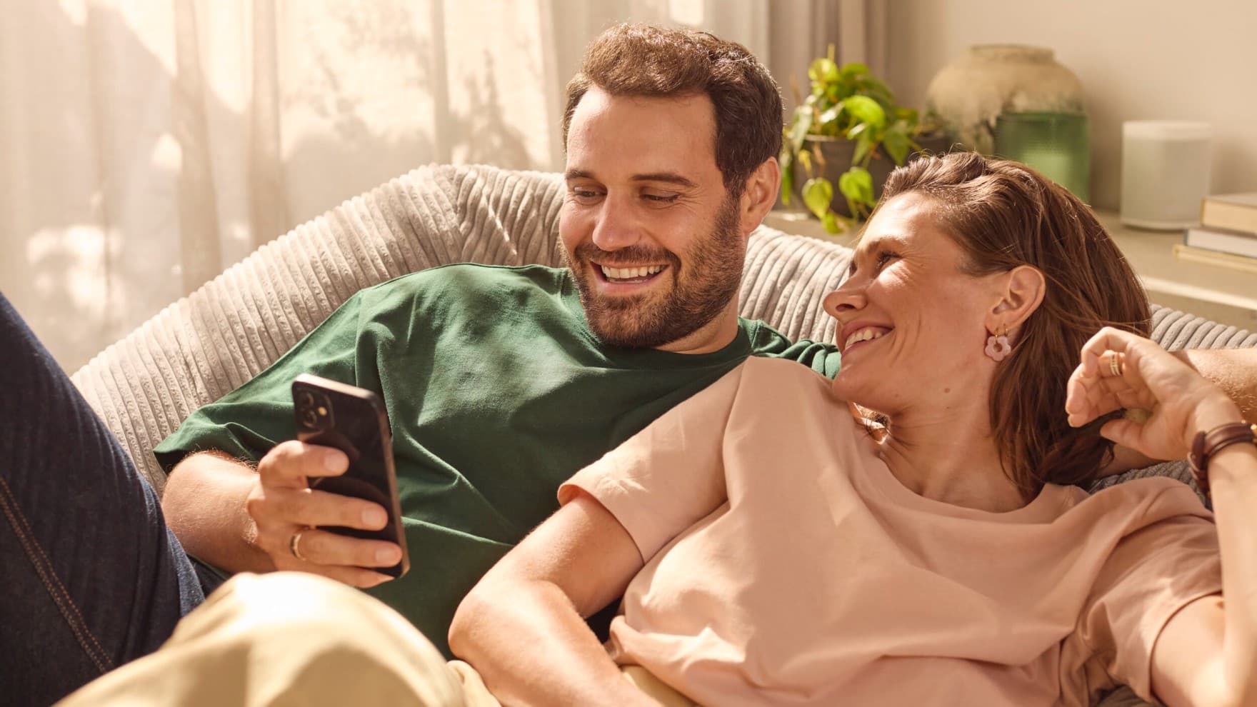 Cuplu asezat pe canapea, uitandu-se la telefon