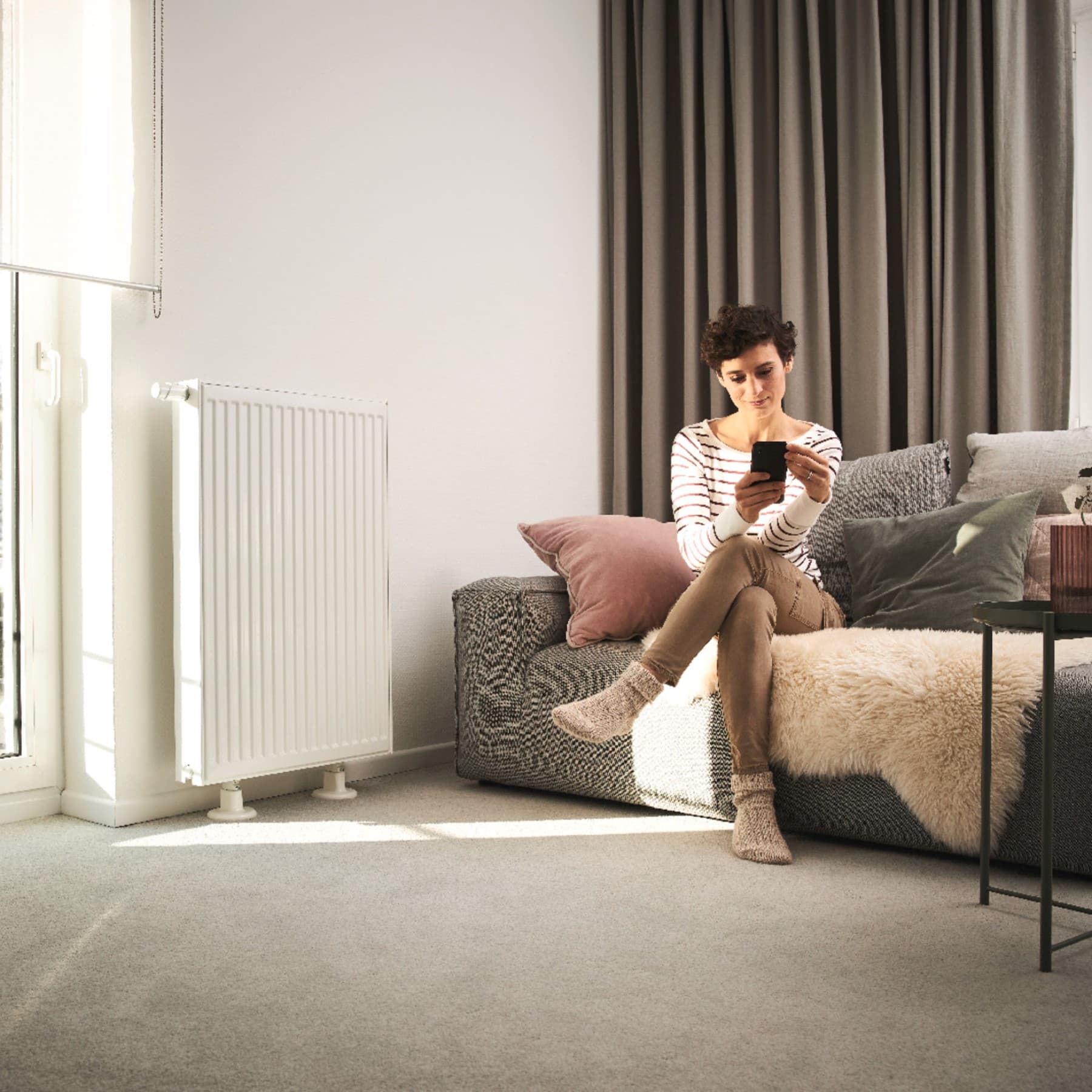 O femeie sta pe canapea langa un radiator