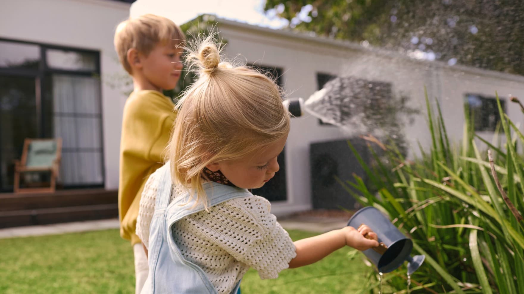 Copii care uda plante intr-o gradina cu o pompa de caldura in fundal