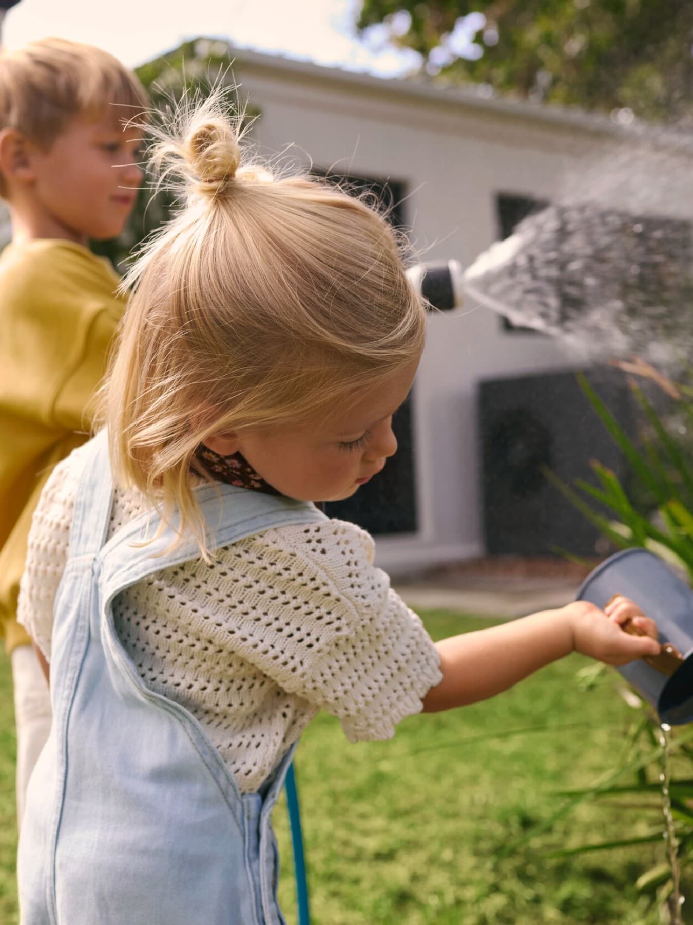Copii care uda plante intr-o gradina cu o pompa de caldura in fundal