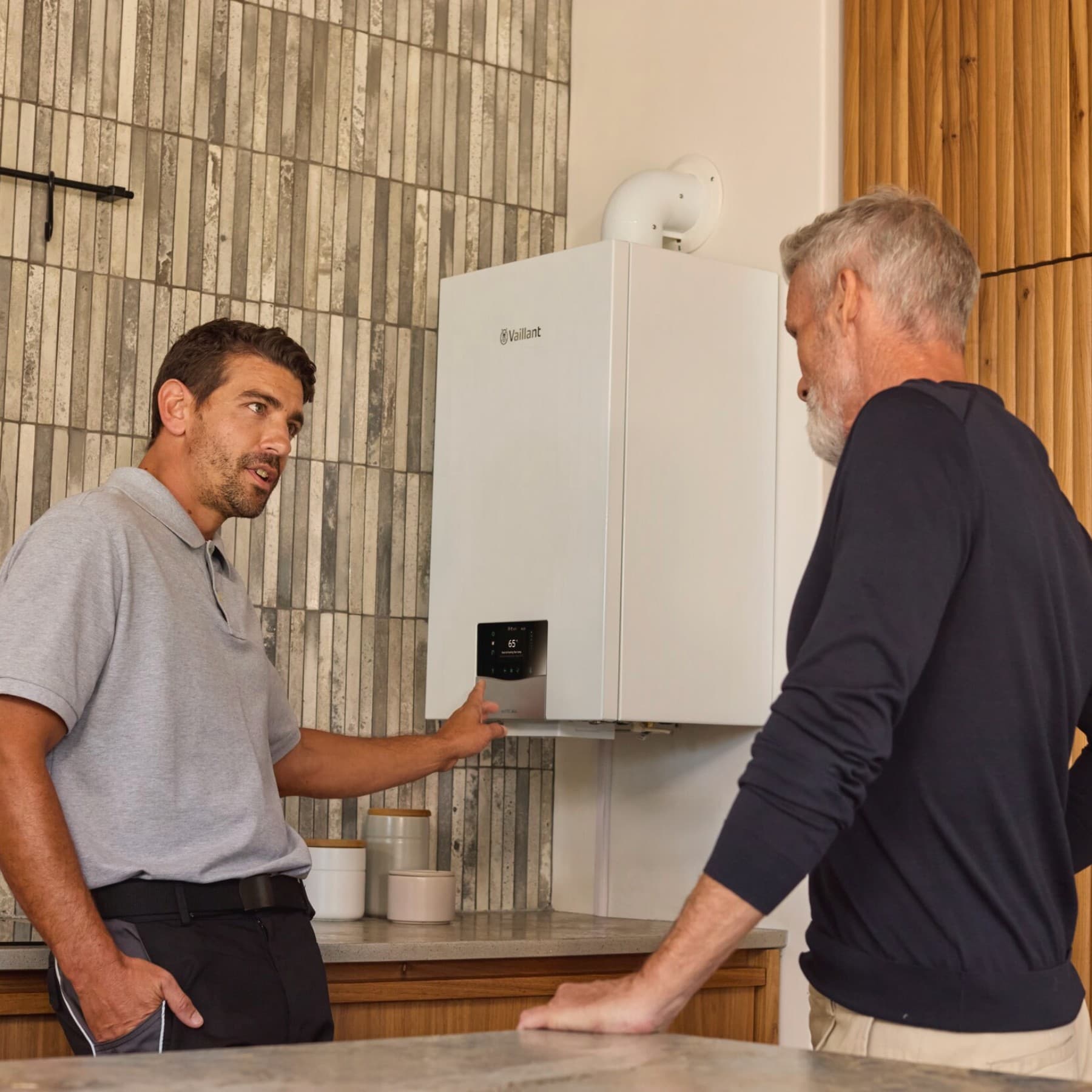 Instalatorul arata spre centrala si vorbeste cu un client
